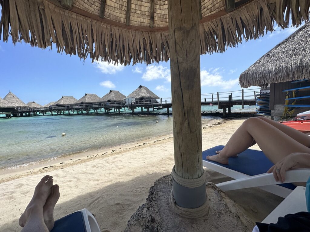 Warm Weather Destinations for custom travel plans: View of overwater bungalows from sun loungers under a palapa on the beach in Moorea