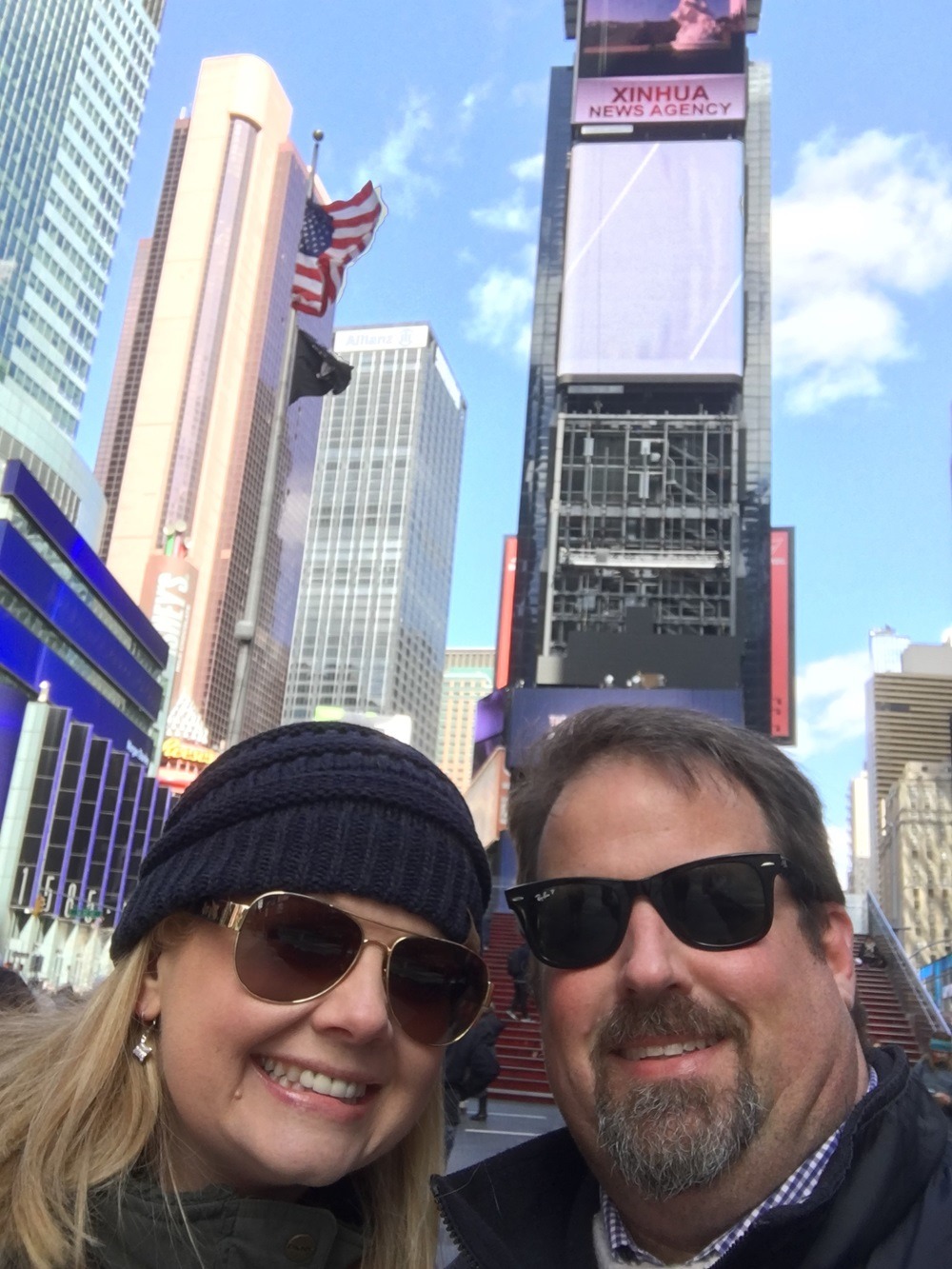 Brandie and John are smiling in a selfie in Times Square in New York City, on another trip that John planned for them