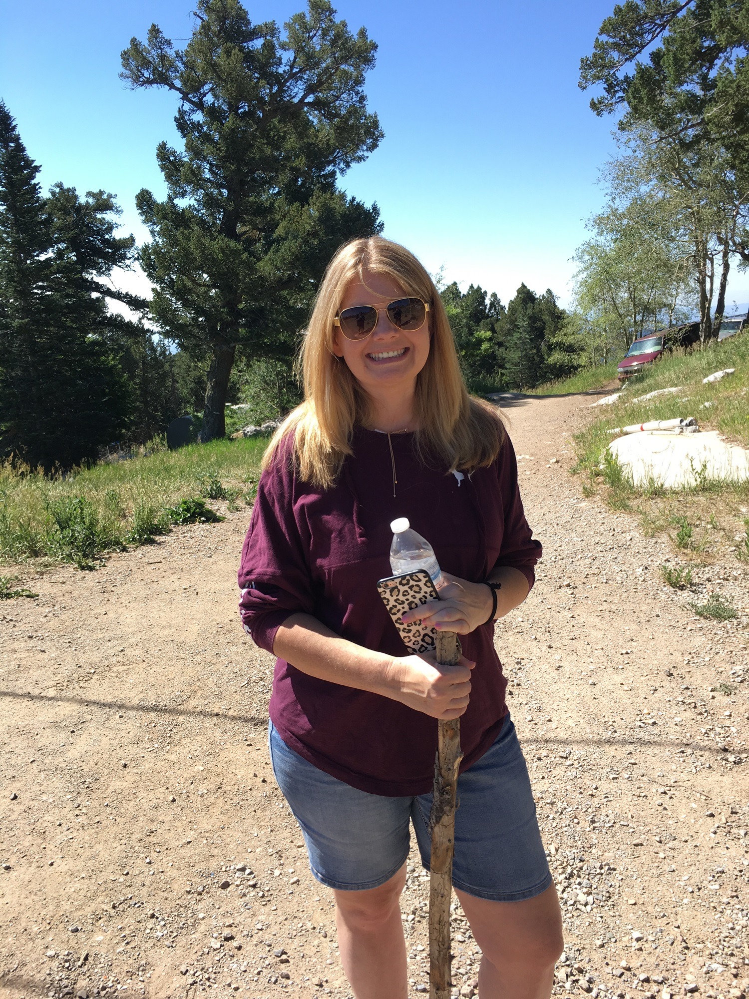 Brandie holding her walking stick on a dusty mountain trail, smiling because she is on another trip she didn’t have to plan