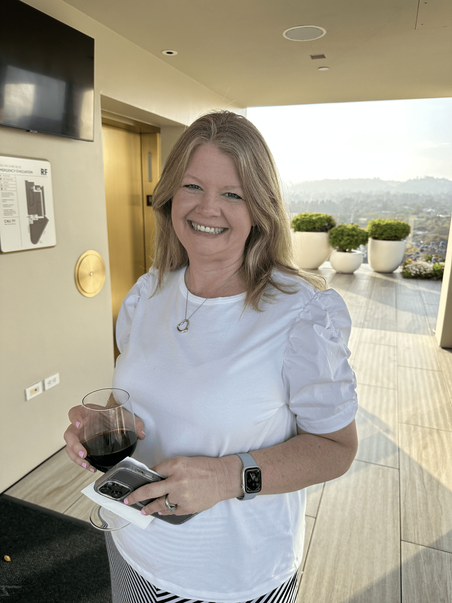 Personal Travel Planner Brandie smiles - she can’t believe she’s here - holding a glass of red wine at the Waldorf Beverly Hills rooftop bar