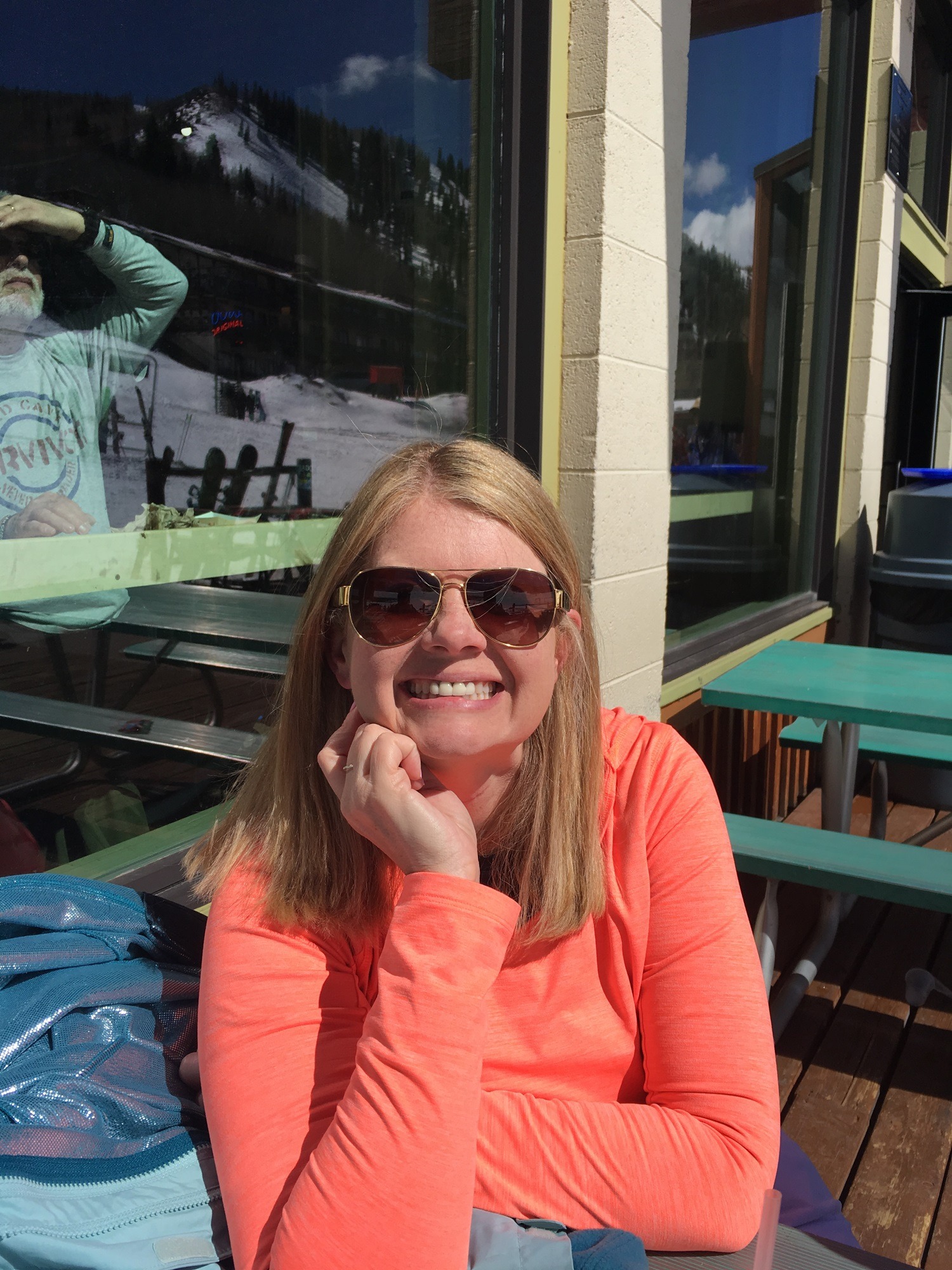 Brandie warming in the sunshine after a day of snow skiing, with a reflection of the ski slopes in the large windows behind her