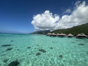 Overwater bungalows perched above coral-dotted crystal blue waters, with mountains behind. It is the Tahiti of your dreams.