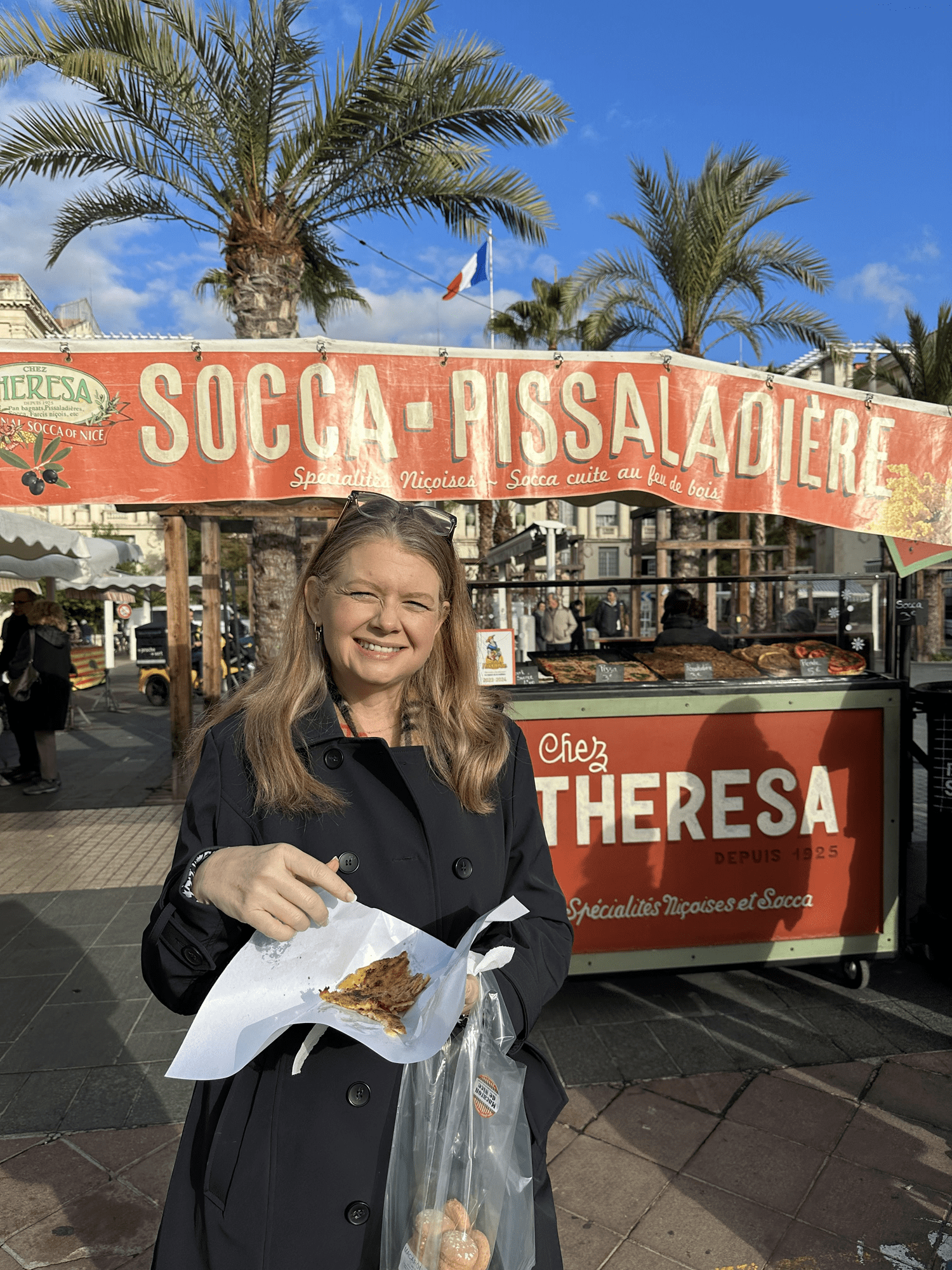Personal Travel Planner Brandie smiling in front of Socca stall in Cours Saleya market in Nice, France, enjoying John’s self-planned food tour
